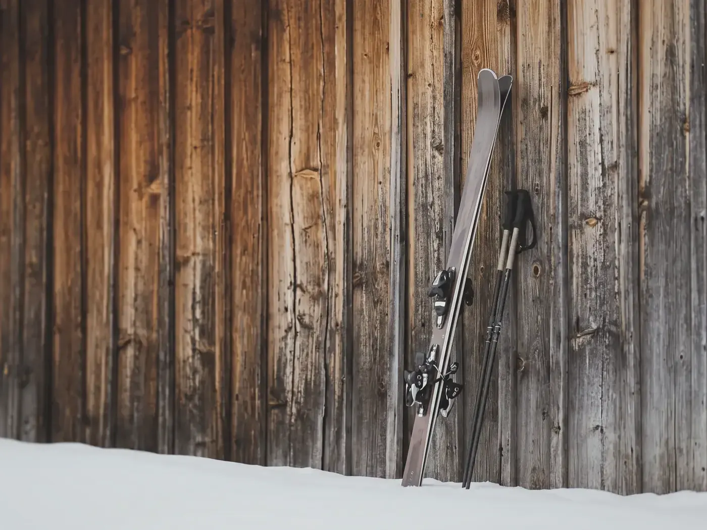 Skis and poles leaning against an old wooden chalet in the snow